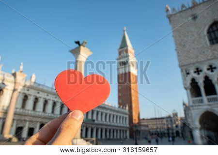 Person's Hand Holding Heart Shape In Front Of Bell Tower