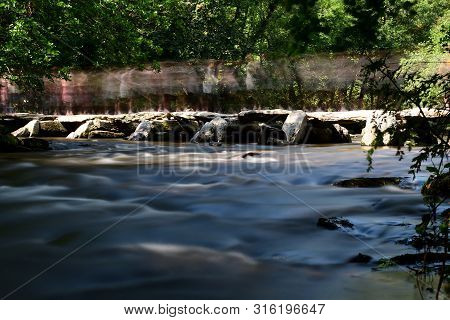 Long Exposure Of The Bridge At Tarr Steps In Devon With Lots Of People On It On A Bank Holiday Monda