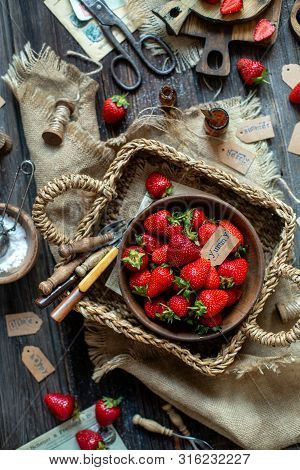 Overhead Shot Of Tasty Ripe Strawberries In Wooden Bowl Stands In Wicker Strawy Basket On Rustic Tab