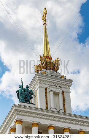 Moscow, Russia - July 22, 2019: Statue Of People Against Golden Spire On The Roof Of Pavilion Ussr I
