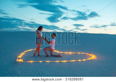The Guy Makes The Girl A Marriage Proposal By Bending His Knee While Standing On The Sand In The Des