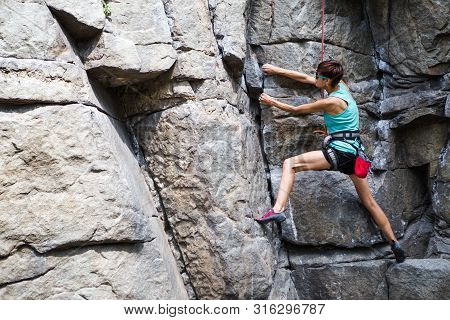 The Girl Climbs The Rock. Rock Climber Is Training On Natural Terrain. Extreme Hobby. A Woman Overco