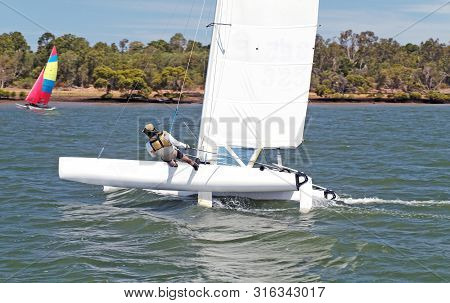 Youth Sailing Small Catamiran Boat With A White Sail On An Inland Waterway. Sailing For Fun And In C