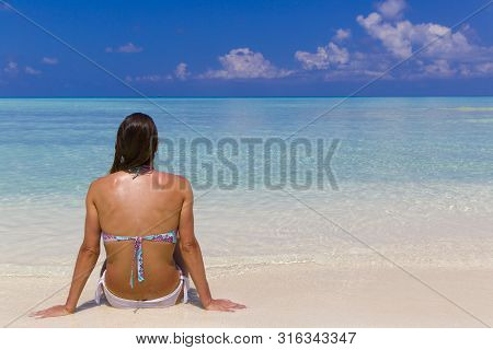 Young Woman Sitting On The Shore In Maldives.