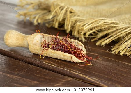 Lot Of Whole Dry Shaffron Thread With Wooden Scoop And Jute Cloth On Brown Wood