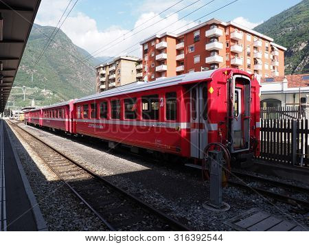 Tirano, Italy On August 2018: Rhaetian Railway Train On Station And Housing Estate In European Itali