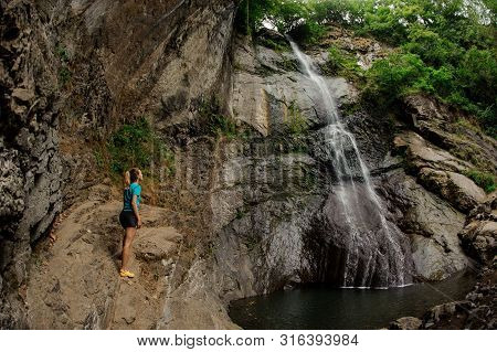 Female Tourist In Sportswear Stands Near Waterfall