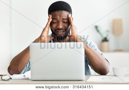 Tired African Freelancer Suffering From Headache Touching His Temple After Hours Of Work On Laptop. 