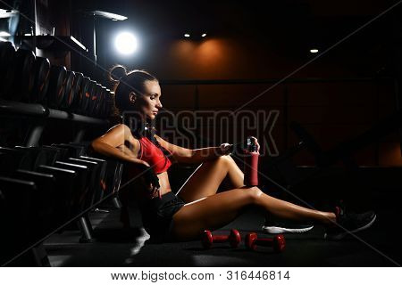 Athletic Girl Fitness Trainer Sitting At Barbells On The Floor In Gym Having A Break Between Exercis