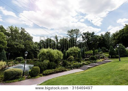 Street Lamps Near Walkway And Bushes In Park With Fountain