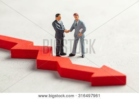 Figurine Of Businessmen Shaking Hands In Suit And Tie And Red Down Arrow. The Concept Of Fictitious 