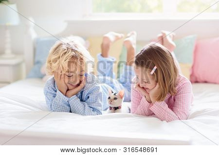 Kids Play In Bed. Children At Home In White Sunny Bedroom. Brother And Sister In Matching Pajamas Pl