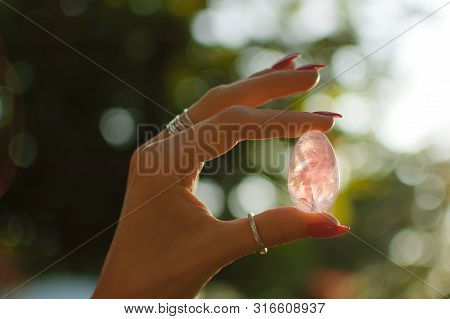 Close Up Photo Of Female Hand With Transparent Amethyst Yoni Egg For Vumbuilding. Quartz Crystal Egg