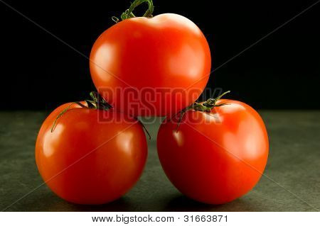 Tres tomates apilados en negro gris de fondo