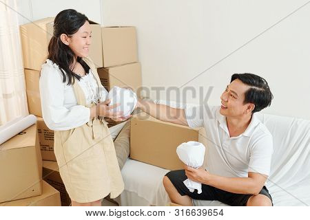 Smiling Father Giving Wrapped Glasses And Cups To His Smiling Teenage Daughter When They Are Unpacki