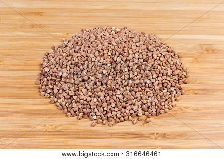 Pile Of Uncooked Brown Pre-steamed Wholegrain Buckwheat Groats Close-up On A Bamboo Wooden Cutting B