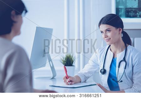 Doctor and patient discussing medical problems in a hospital consulting room. Doc filling in a patient's form