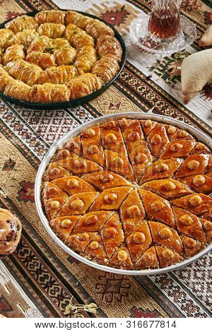Beautiful Serving Homemade Baklava in a Round Metal Tray on Vintage Traditional Tablecloth. Sweet Turkish Style Brown Glazed Pastries Baklawa with Walnut, Nuts, Sugar, Pistachio and Honey Close Up