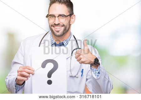 Handsome young doctor man holding paper with question mark over isolated background happy with big smile doing ok sign, thumb up with fingers, excellent sign