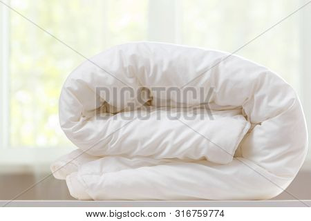 A Folded White Duvet Lies On A Table On A Blurred Background.