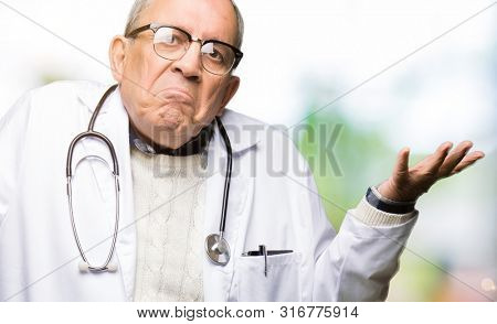 Handsome senior doctor man wearing medical coat clueless and confused expression with arms and hands raised. Doubt concept.
