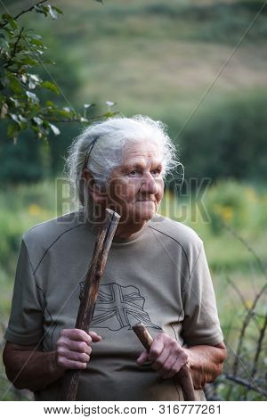Portrait Of An Old Woman With Arthritic Feet Walking In A Grassy Meadow Leaning On A Stick As A Cane