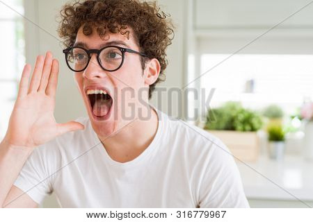 Young handsome man wearing glasses shouting and screaming loud to side with hand on mouth. Communication concept.