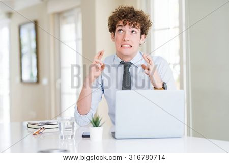 Young business man working with computer laptop at the office smiling crossing fingers with hope and eyes closed. Luck and superstitious concept.