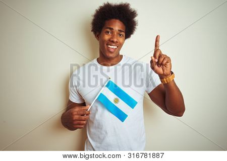Afro american tourist man holding Argentinian Argentina flag over isolated white background surprised with an idea or question pointing finger with happy face, number one