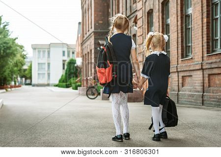 Back To School, Portrait From The Back Of Elementary School Students With Backpacks In Uniform Holdi