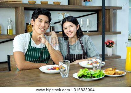 Portrait Of Cute Happy Couple In Aporn Jposting To Have Breakfast Decorated With Salad And Orange Ju