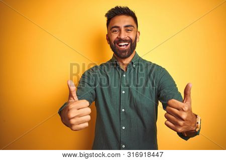 Young indian businessman wearing elegant shirt standing over isolated white background success sign doing positive gesture with hand, thumbs up smiling and happy. Cheerful expression