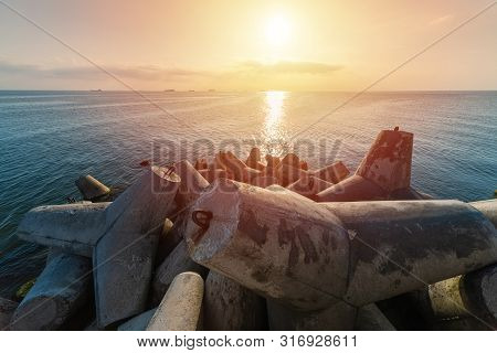 Beautiful Sunset Seascape. Breakwaters Tetrapods Ashore Of Pier. Cargo Ships On The Horizon. Travel 