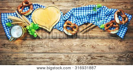 Rustic background for Oktoberfest or Bavarian specialties with white and blue fabric, hop, silverware, beer glass and pretzels on wooden table. Menu card for Restaurants