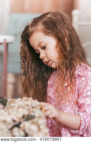 A Little Pretty Girl With Fornic Hair Looks At The Flowers. Vertical Portrait