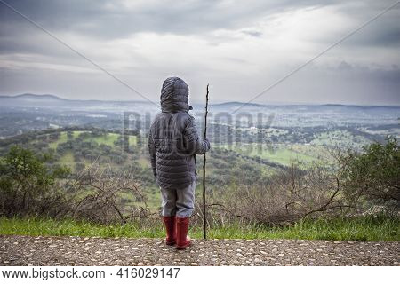 Child Boy Observing The Dehesa Landscape Outskirts Alburquerque, Extremadura, Spain. He Holds A Cane