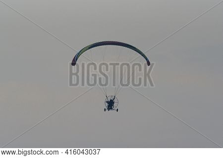 Silhouette Of The Paramotor Gliding And Flying In The Air Through Soft Sunlight Sky