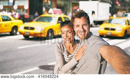 New York travel selfie tourists couple taking photo on NYC city street summer holiday vacation with yellow taxi cabs in the background. Man and woman friends having fun.