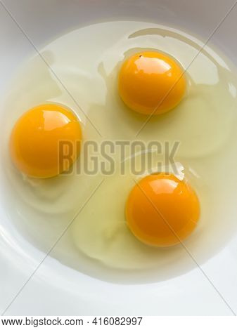 Three bright yellow raw chicken eggs in a white bowl.