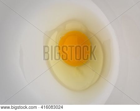 One bright yellow raw chicken egg in a white bowl.