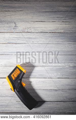 Yellow-black Pyrometer On A Wooden Background. A Device For Non-contact Temperature Measurement. Stu