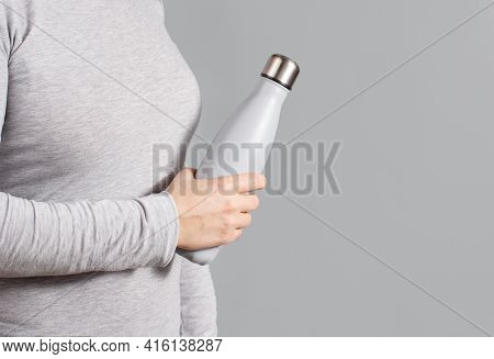 Woman In Grey Tee Holding Grey Insulated Bottle On Grey Background Close Up