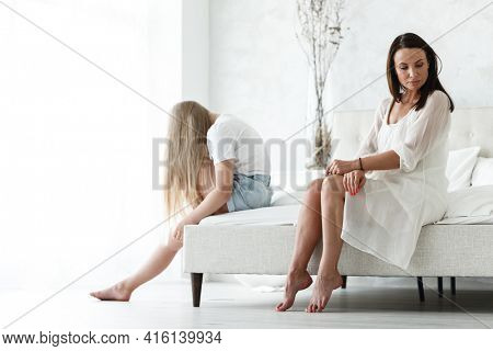 Family conflict and relations concept. Mother and daughter having quarrel and aguring at home. Sad woman and teenage girl sitting on bed. Not looking at each other.