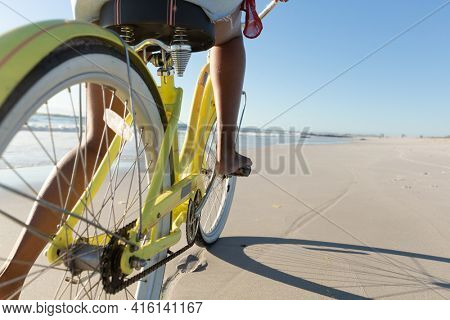 Low section of mixed race woman on beach holiday riding bicycle on the sand by the sea. outdoor leisure vacation time by the sea.