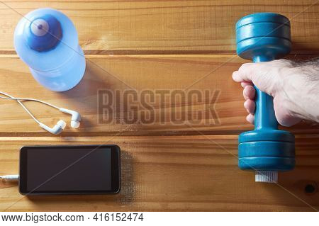 Fitness Equipment At Home, Top View Of Hand Holding Dumbbell, Water Bottle And Mobile Phone With Ear