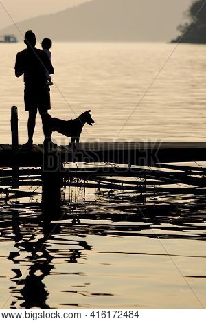 Koh Chang Island. Thailand - 21/01/2016: Silhouettes Of A Man Holding His Child  And A Dog Standing 