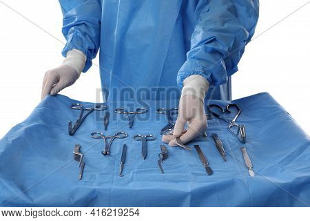 Doctor Holding Pott's Scissors Near Table With Different Surgical Instruments On Light Background, C