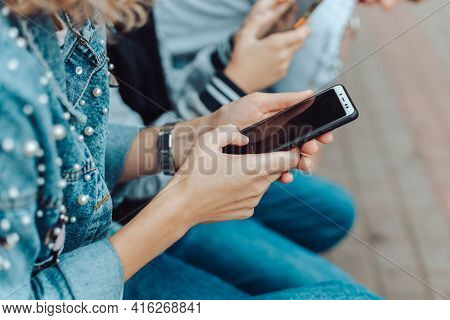 People Use A Smartphone While Sitting On A Bench In The Street.