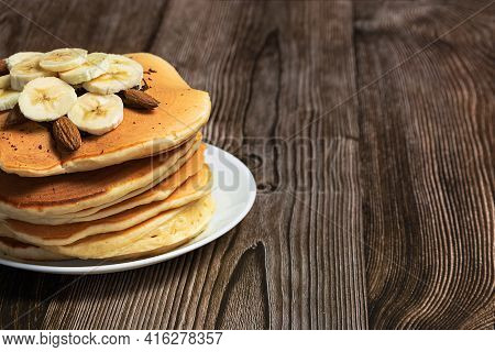 Pancakes With Bananas And Nuts, On A Dark Wooden Background, In A Close-up, With A Place For An Insc