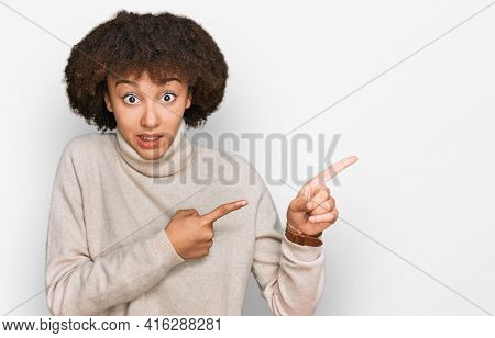 Young hispanic girl wearing wool winter sweater pointing aside worried and nervous with both hands, concerned and surprised expression 